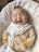 A smiling baby wearing cozy clothes sitting on a soft blanket.