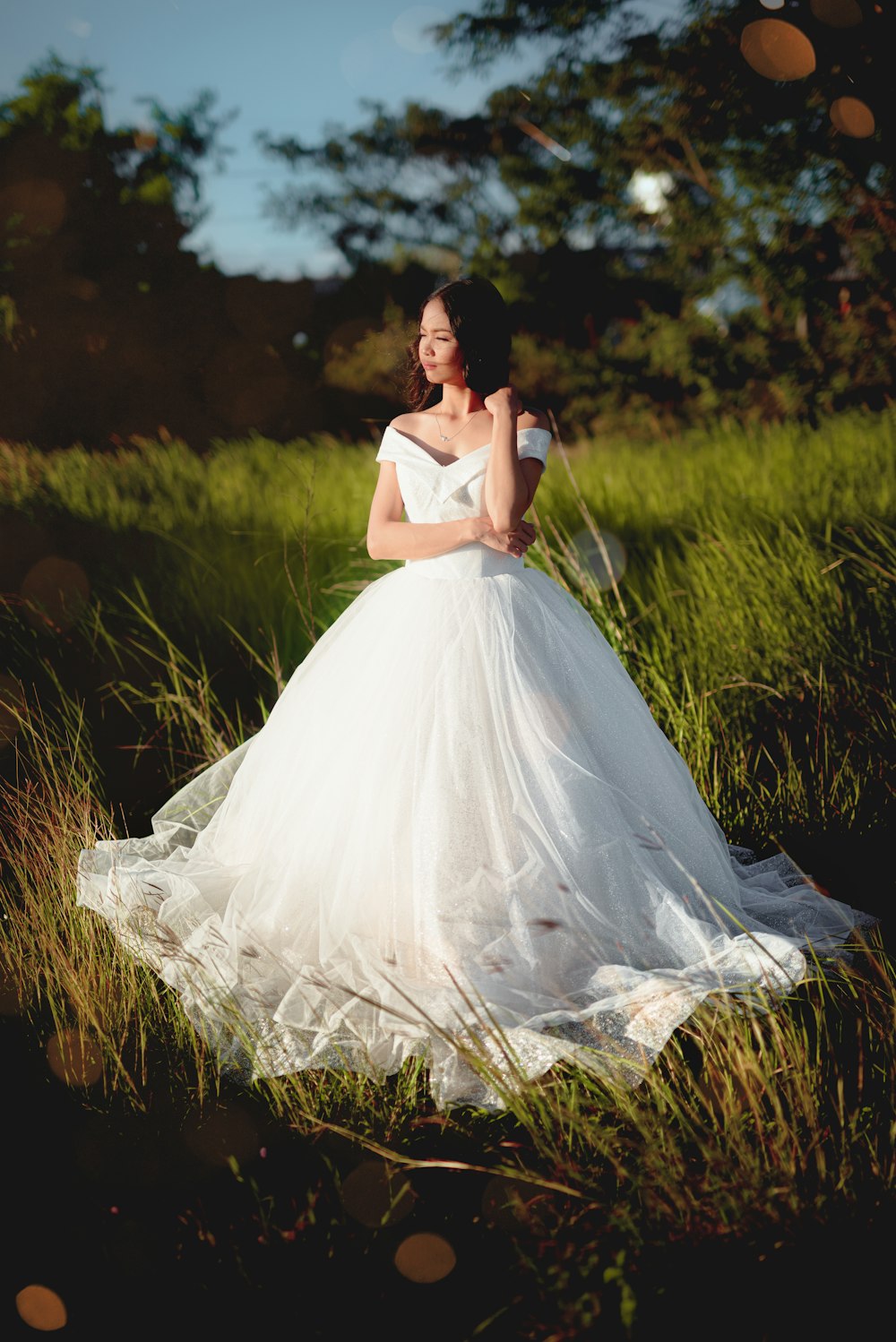 femme en robe blanche debout sur le champ d’herbe verte pendant la journée