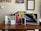 A collection of Apple product boxes displayed on a wooden desk, including an iPad, MacBook, iPhone, Apple Pencil, and AirPods. There are writing implements and a small plant in the background, with congratulatory certificates and a motivational poster on the wall.