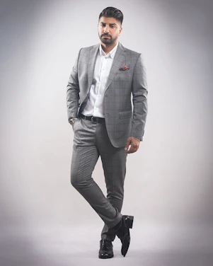 A confident man dressed stylishly against a soft gray background.