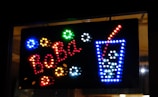 A brightly colored LED sign features the word 'BOBA' in red lights on a black background. To the right, a depiction of a tall drink cup outlined in blue lights with white lights representing ice or bubbles, and a red straw emerging from the top.