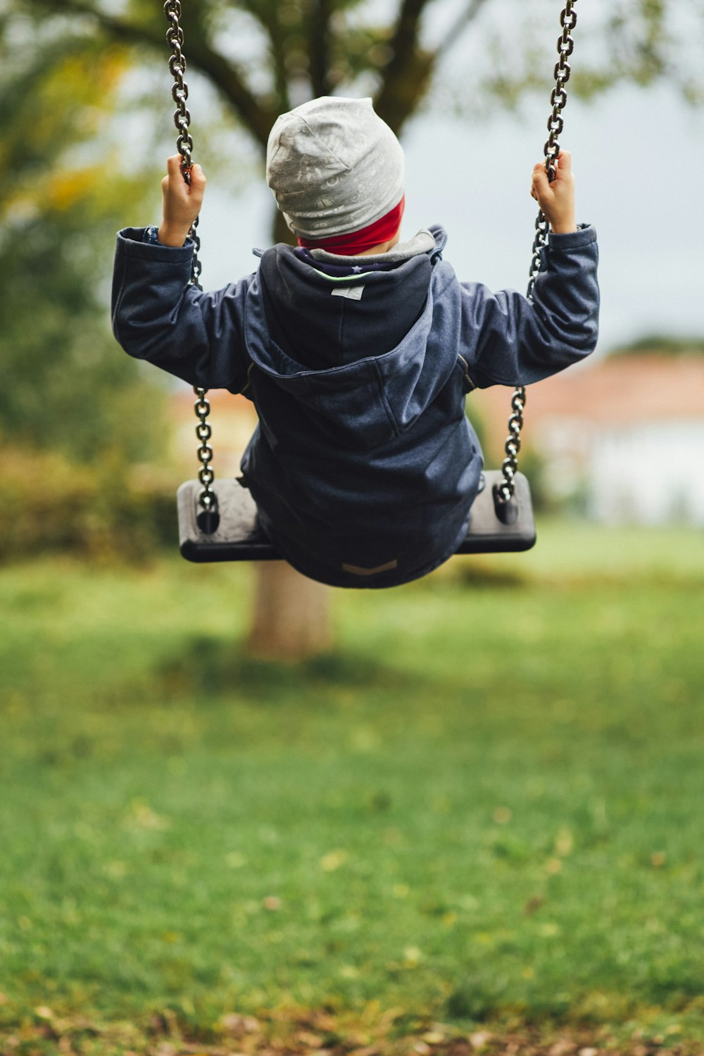 child in gray long sleeve shirt sitting on swing during daytime