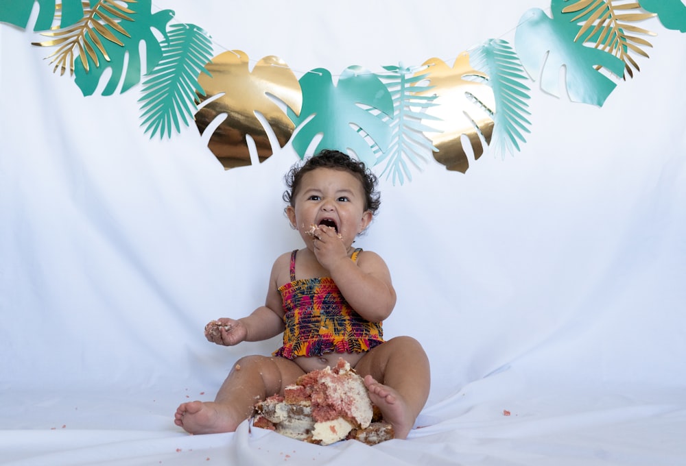 baby in red and white tank top sitting on white textile