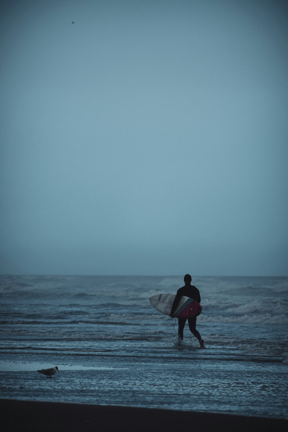 man in red shirt holding white surfboard walking on beach during daytime