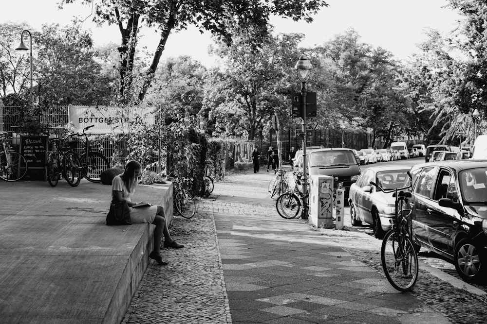 grayscale photo of man and woman sitting on bench near road
