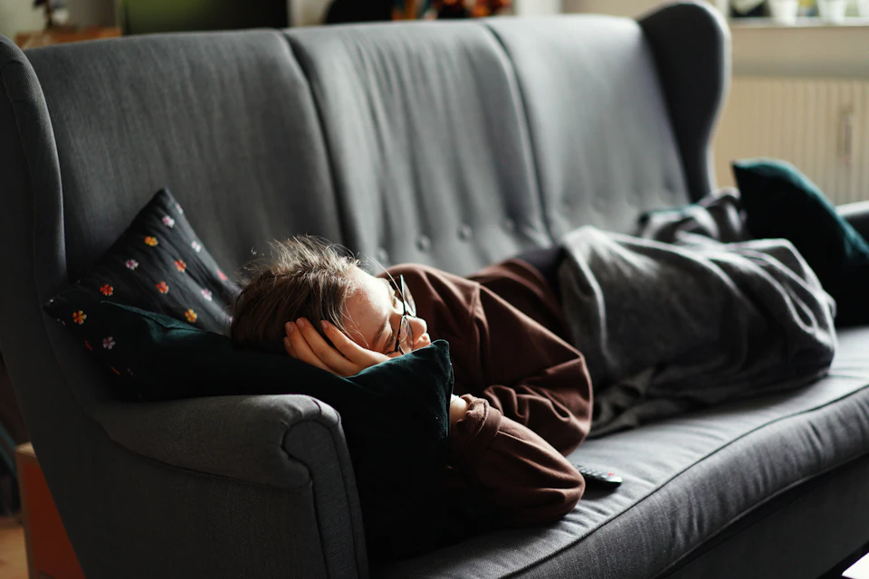 Person lying on gray couch with head on black pillow and arms stretched out
