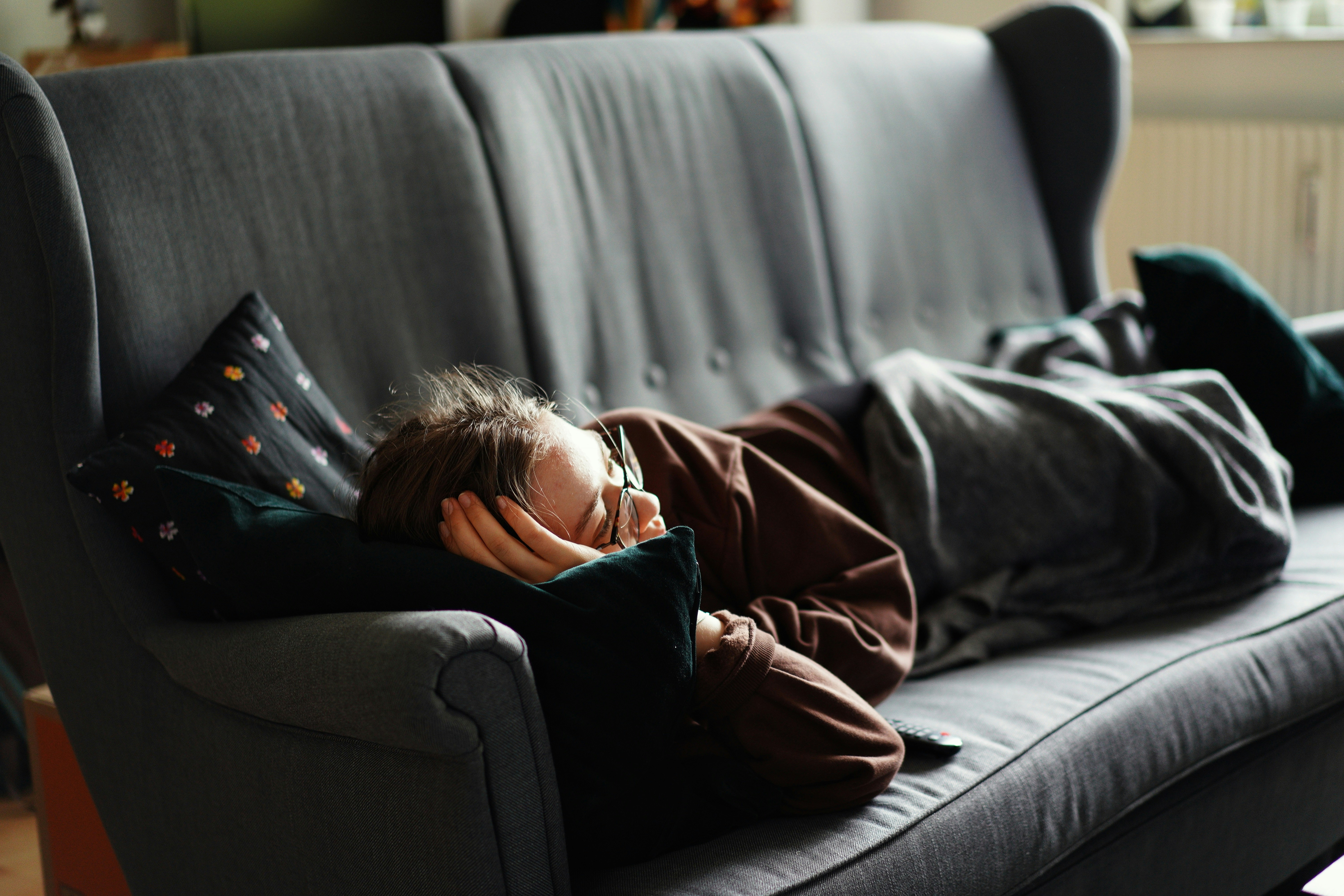 woman in pink jacket lying on gray couch