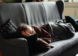 woman in pink jacket lying on gray couch