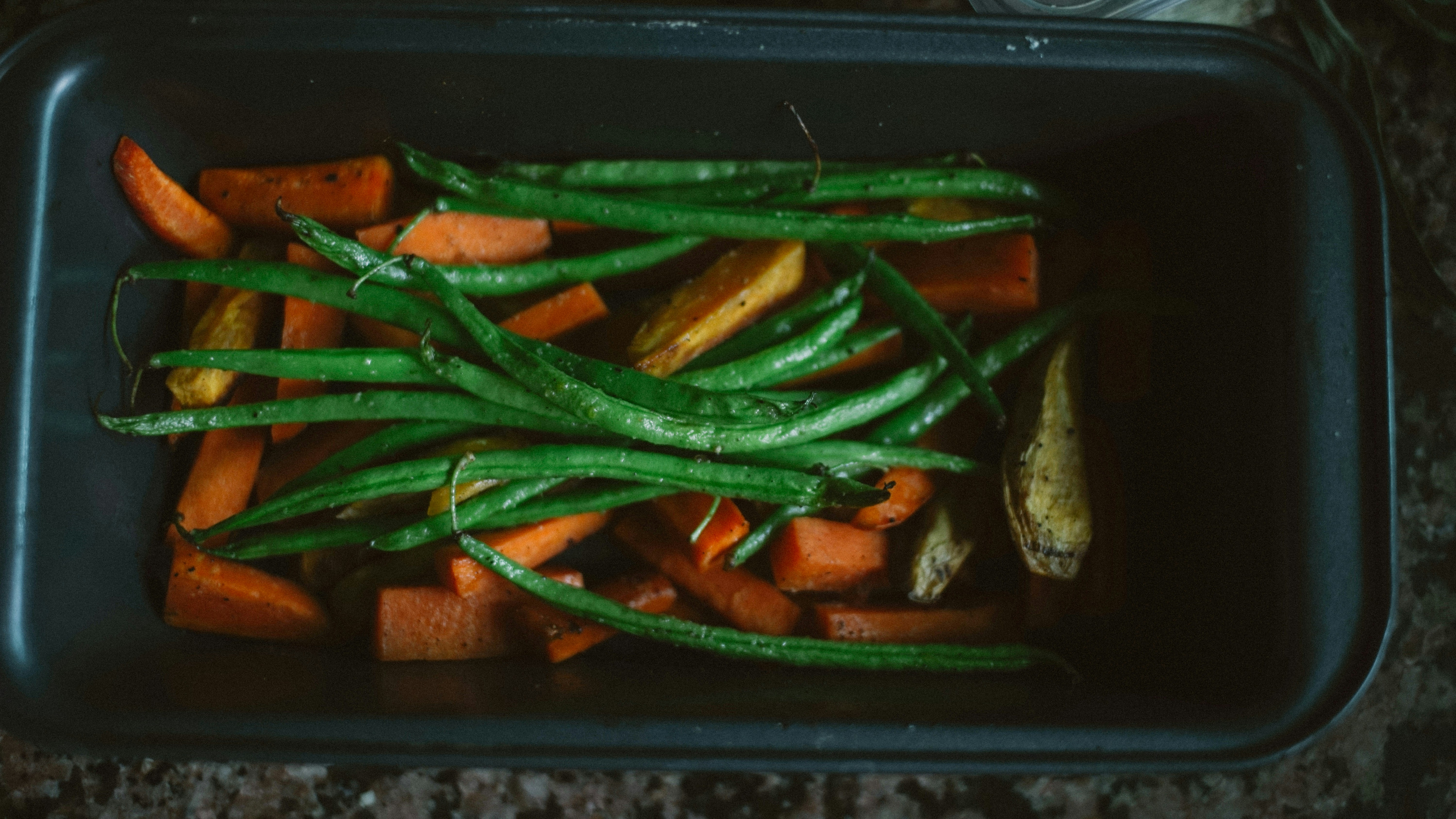 A family kitchen counter organized with fresh seasonal vegetables, a digital tablet showing a meal plan, and school lunchboxes being packed.