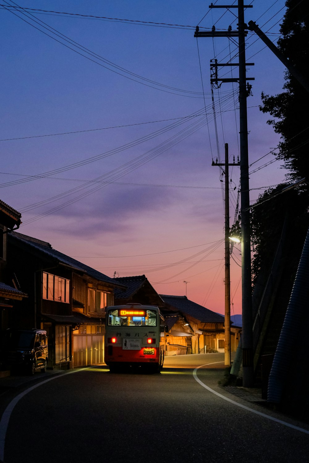 昼間、茶色の建物の脇に停車する赤いバン