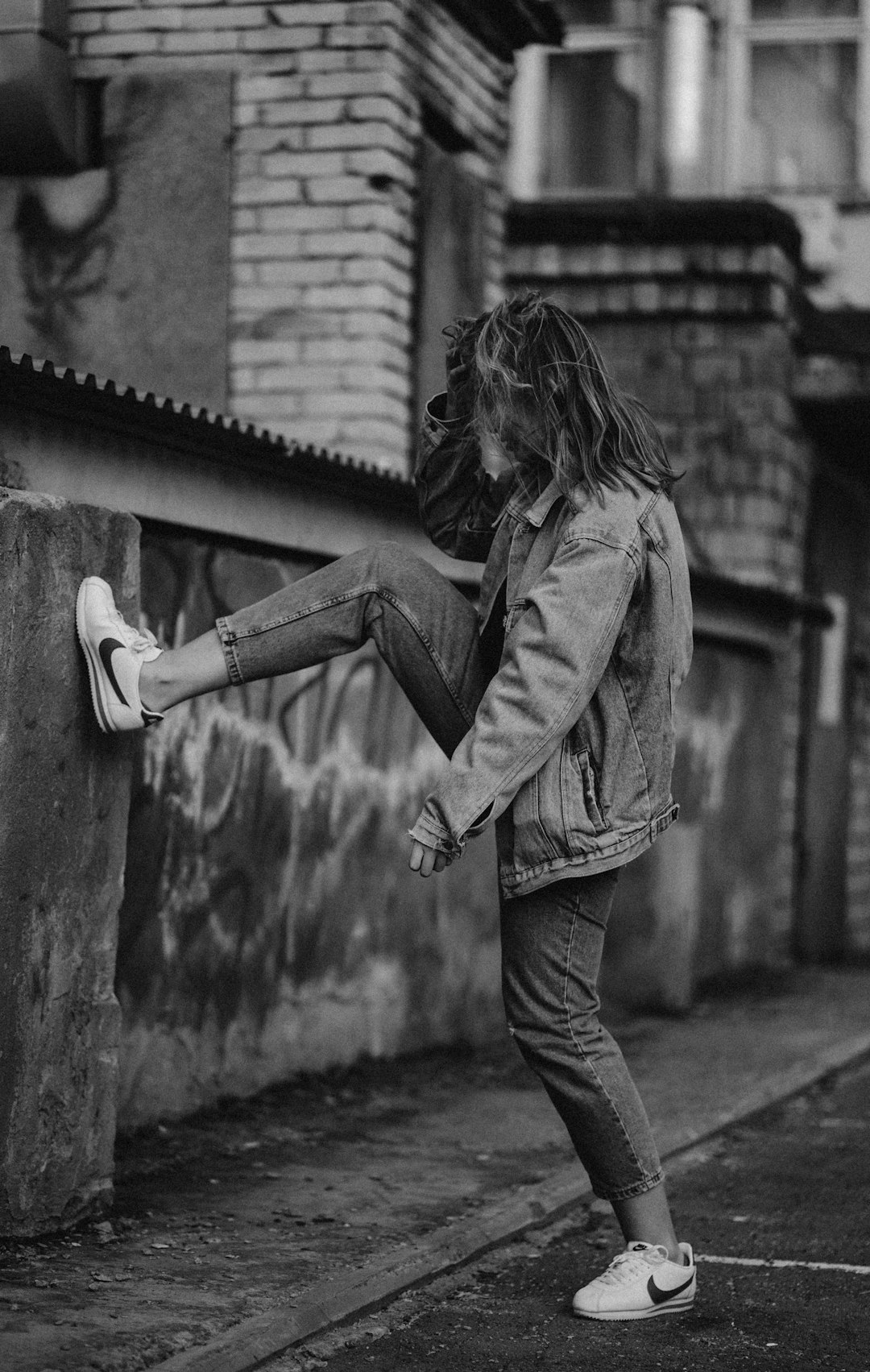 woman in jacket and pants leaning on wall