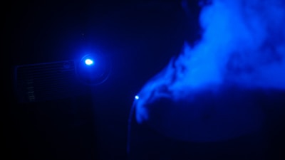 A projector displaying a movie on a blank wall in a dark room.
