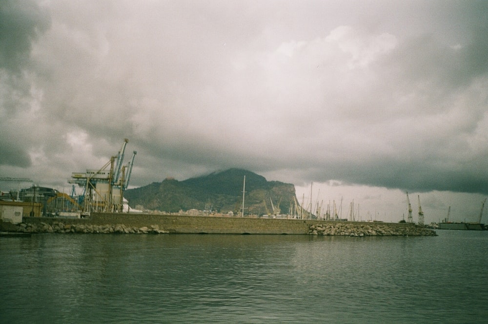 body of water near mountain under cloudy sky during daytime