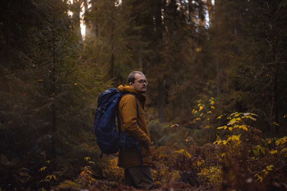 man in brown jacket and black backpack standing in forest during daytime