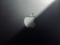 A minimalist design featuring a metallic surface with a prominent logo shaped like an apple with a bite taken out of it. The lighting creates a gradient effect, adding a sleek and modern aesthetic.