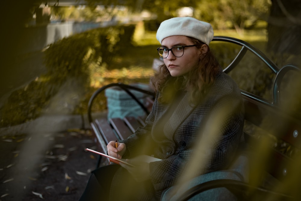 woman in white knit cap and gray jacket sitting on black metal bench during daytime