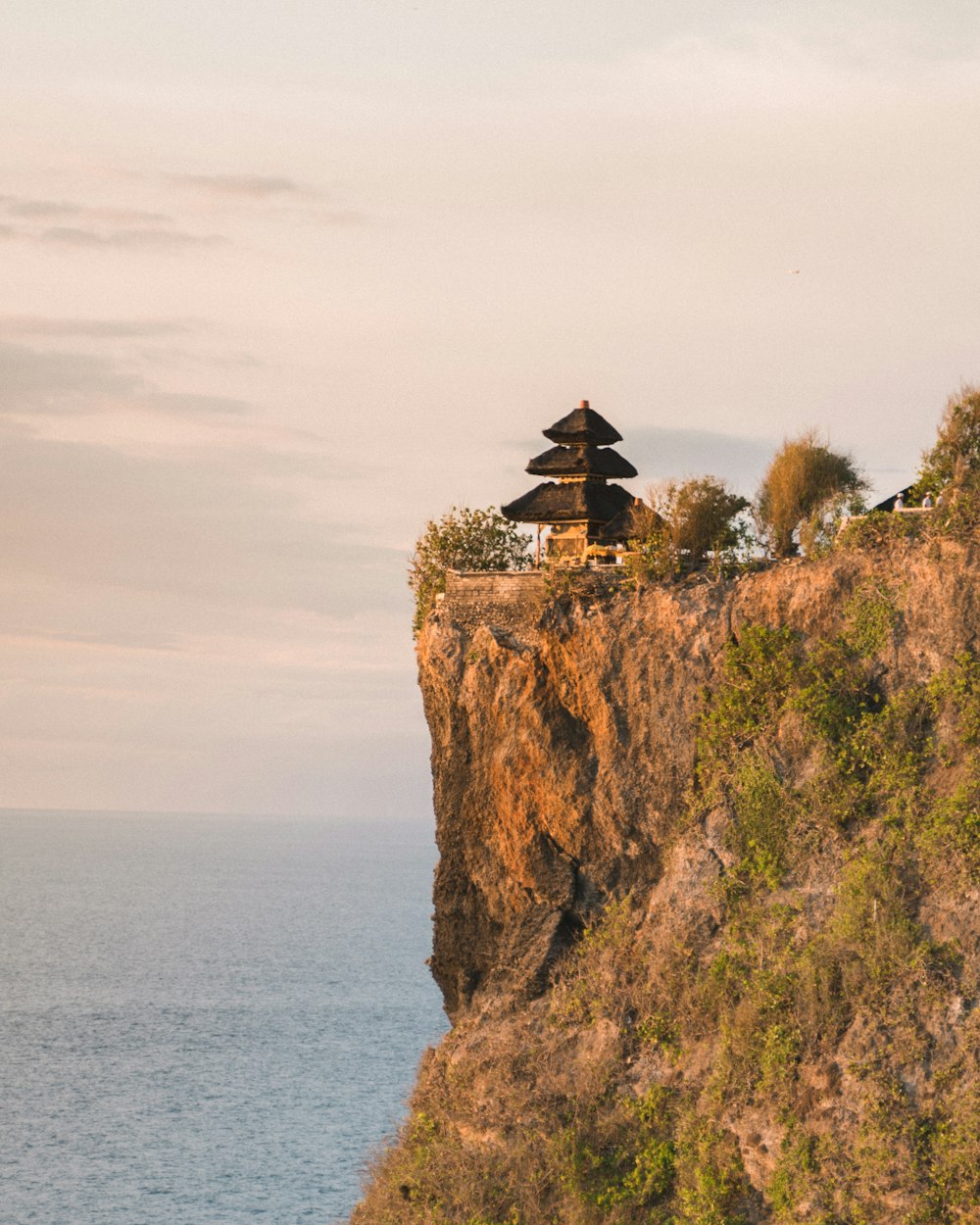 casa de madeira marrom na formação rochosa marrom perto do corpo de água durante o dia