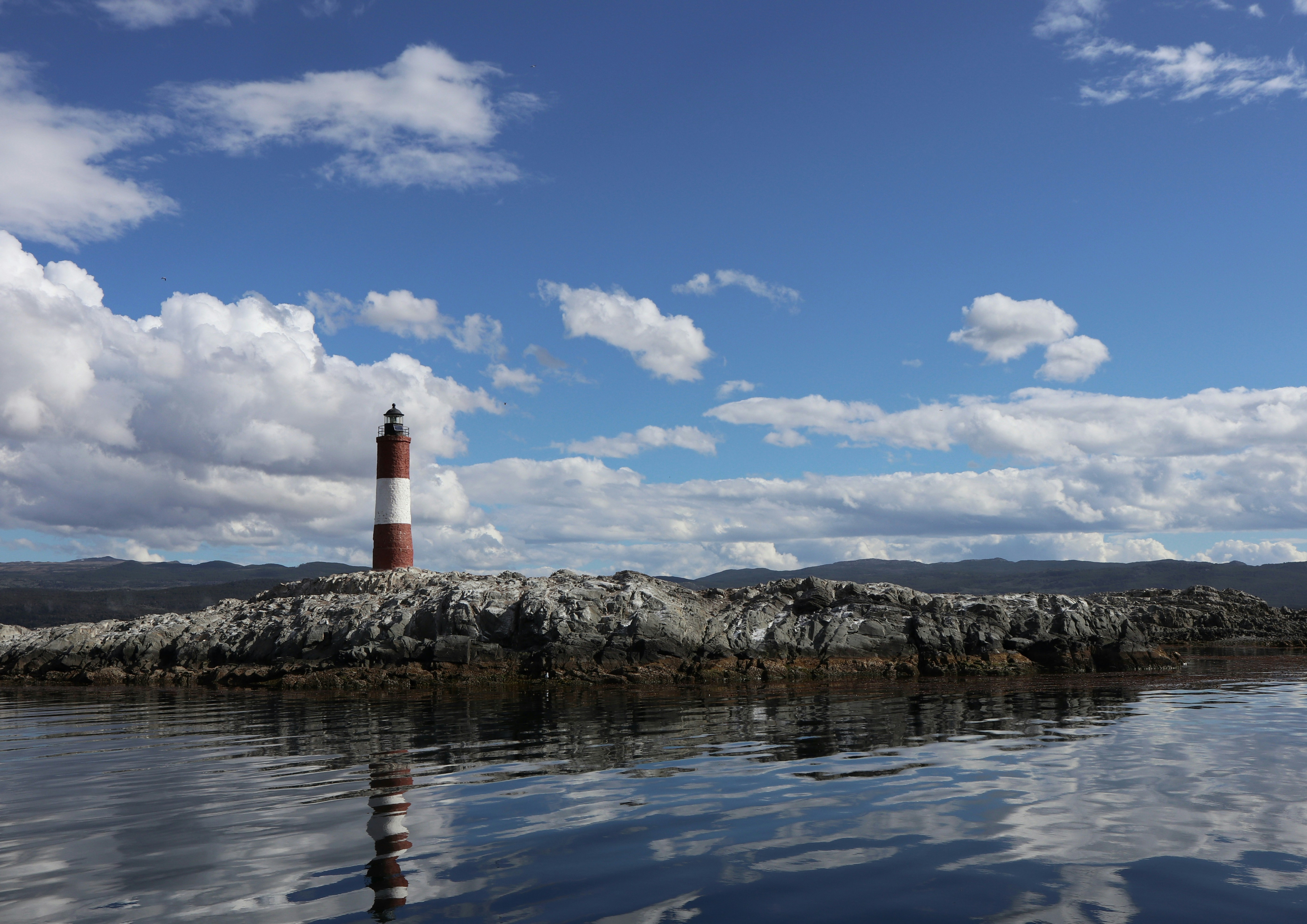 red and white lighthouse on rocky shore under blue and white sunny cloudy sky during daytime