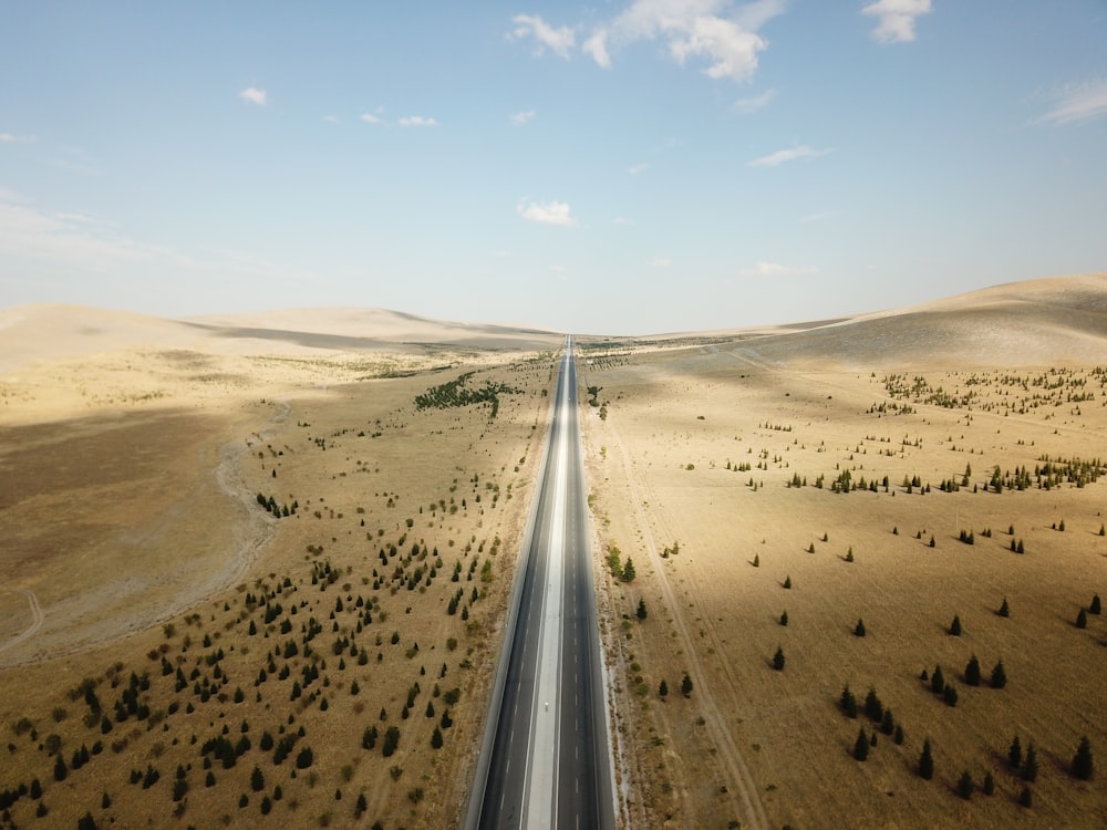 gray asphalt road between brown sand under blue sky during daytime