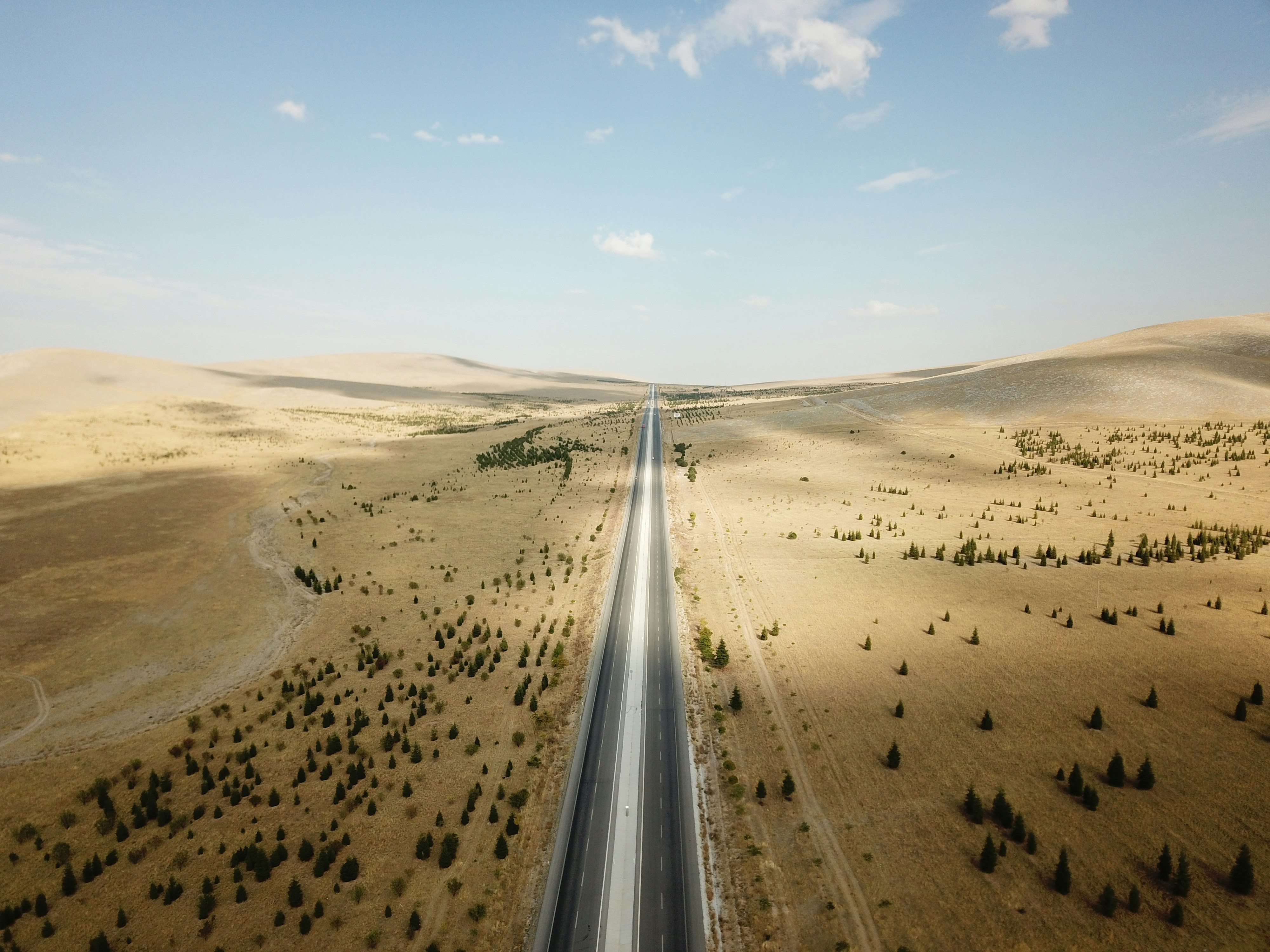 gray-asphalt-road-between-brown-sand-under-blue-sky-during-daytime