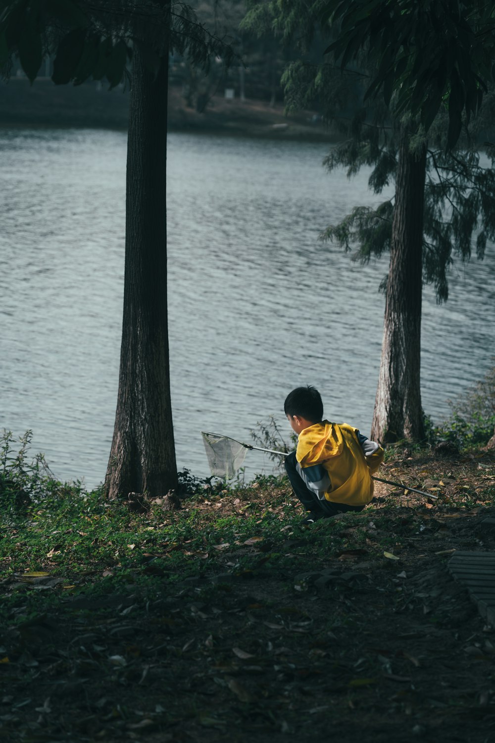노란색과 검은색 재킷을 입은 남자가 수역 근처의 갈색 나무 줄기에 앉아 있다