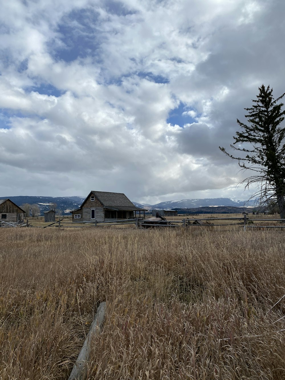 brown wooden house near green grass field under white clouds and blue sky during daytime