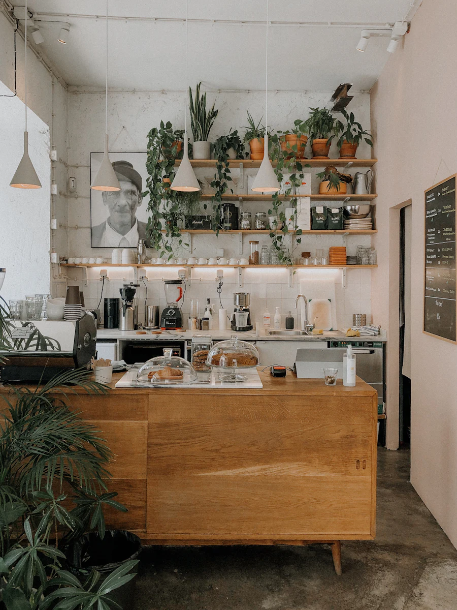 A working café counter: cake domes, a grinder and shelves of equipment against white tile.
