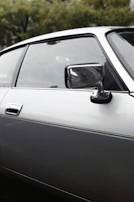 A sleek black side mirror attached to a shiny car door, capturing sunlight and nearby trees.