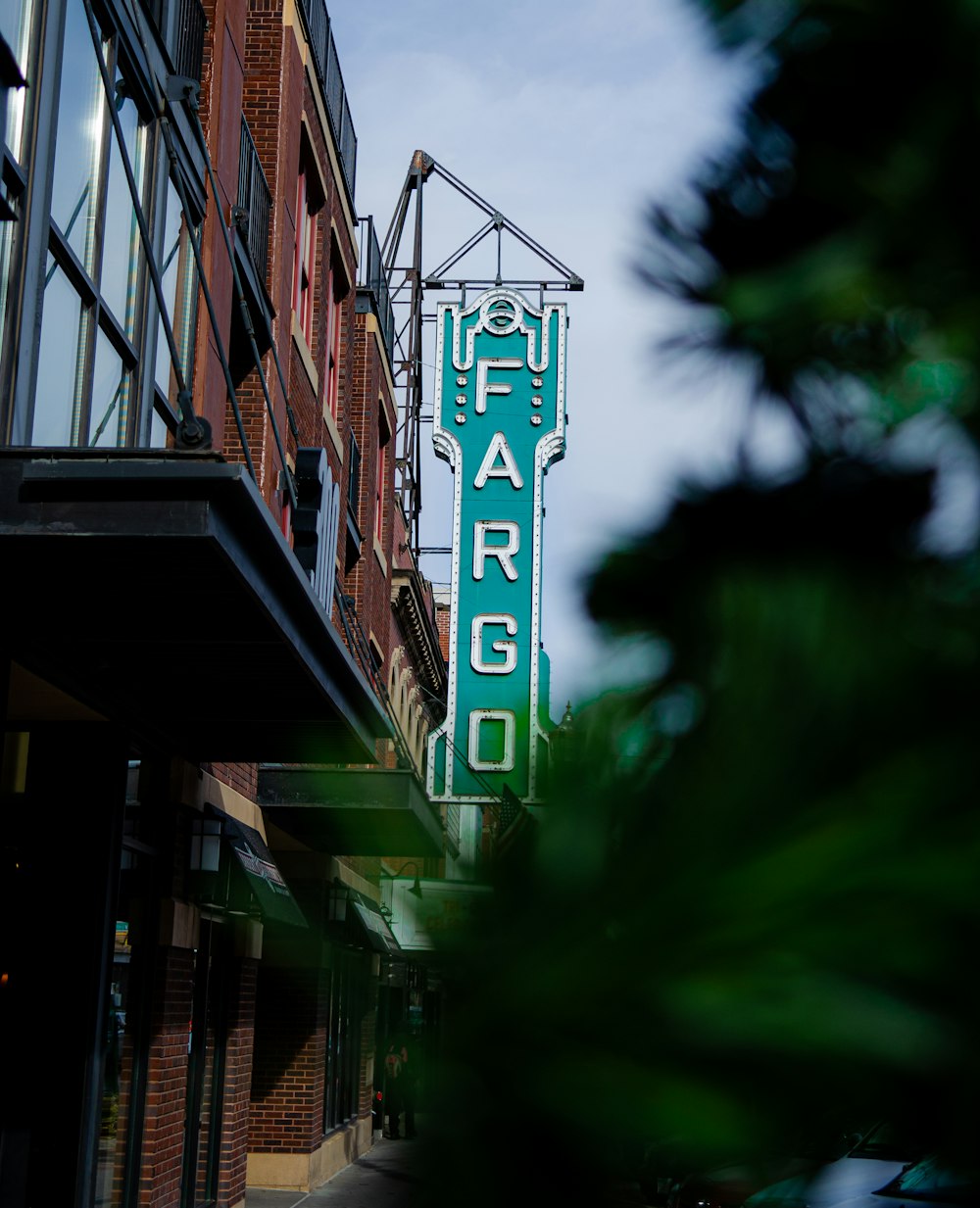 Vertical, green Fargo theater sign photographed through tree leaves