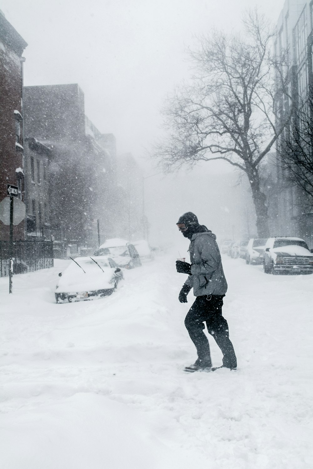 uomo in giacca grigia e pantaloni neri che cammina sulla strada coperta di neve durante il giorno