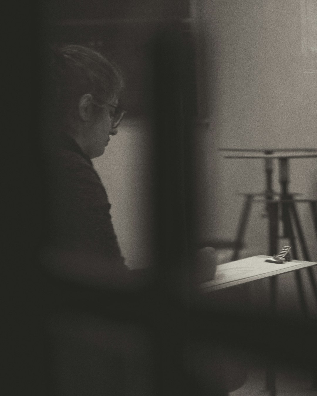 grayscale photo of man in eyeglasses looking at the window