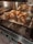 Five golden-brown croissants are baking in an oven, placed on a baking tray lined with parchment paper. The oven has a sleek, digital control panel with several icons and a timer displaying '00:05'. The interior is well-lit, highlighting the texture of the pastries.