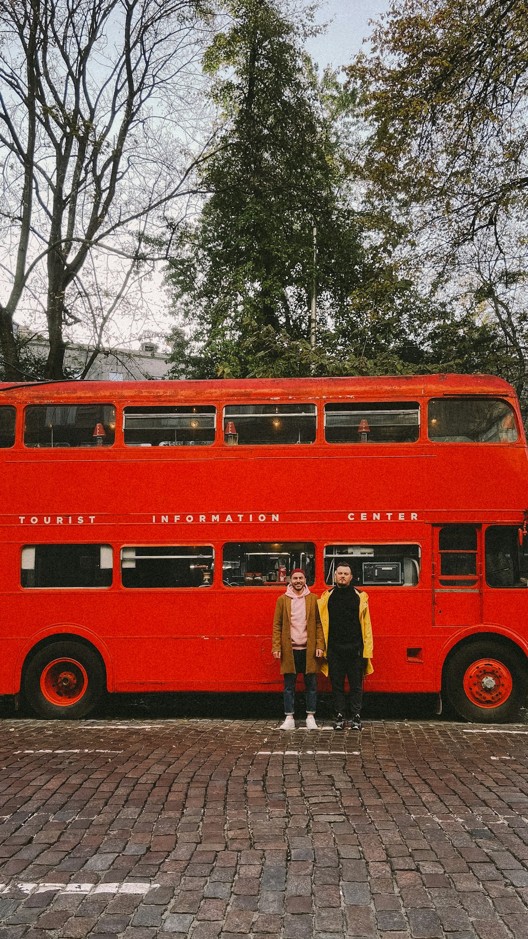 man in black jacket standing beside red bus during daytime
