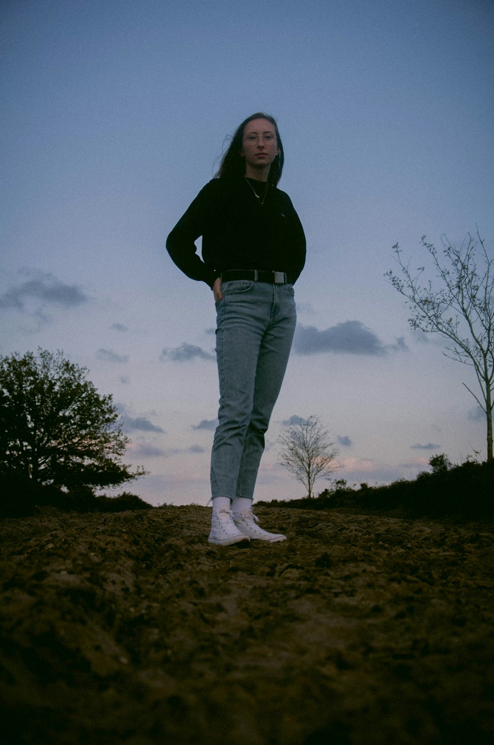 woman in black jacket and blue denim jeans standing on brown field