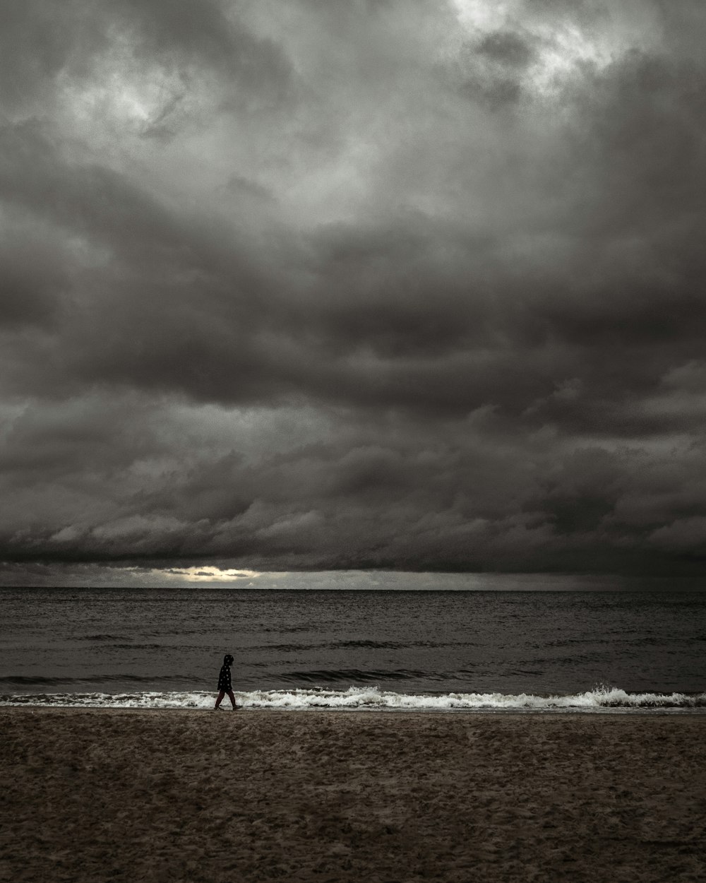 pessoa andando na praia sob o céu nublado durante o dia