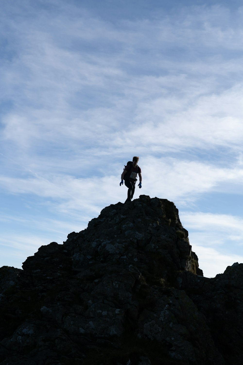 man in black jacket standing on rock formation under white clouds and blue sky during daytime