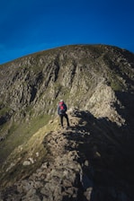 A hiker adjusting their backpack straps on a rocky mountain trail under a clear blue sky.