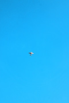 A small airplane is flying high in the sky against a clear blue background. The plane appears to be a light aircraft with a simple design.