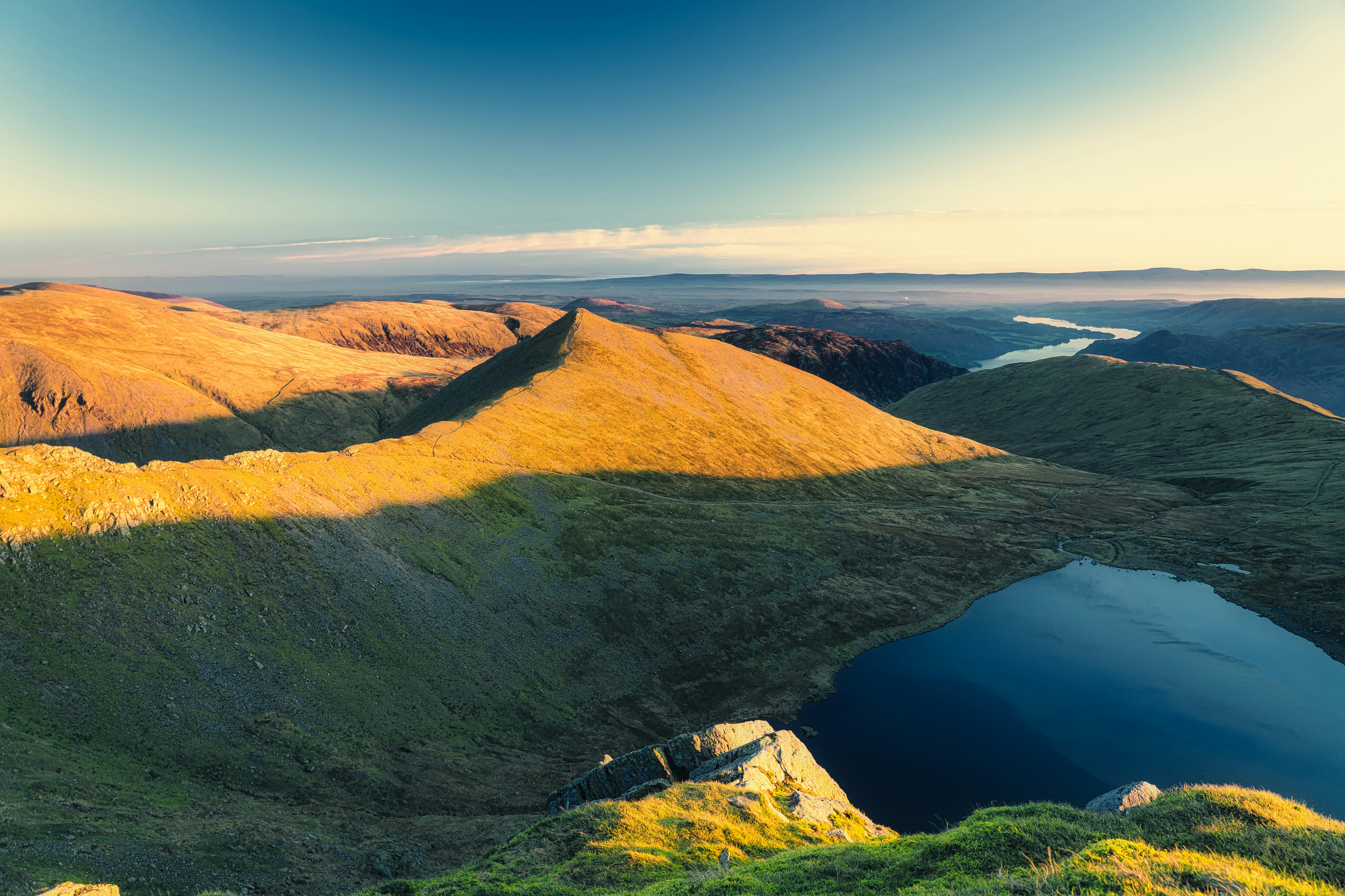brown and green mountain beside blue lake under blue sky during daytime