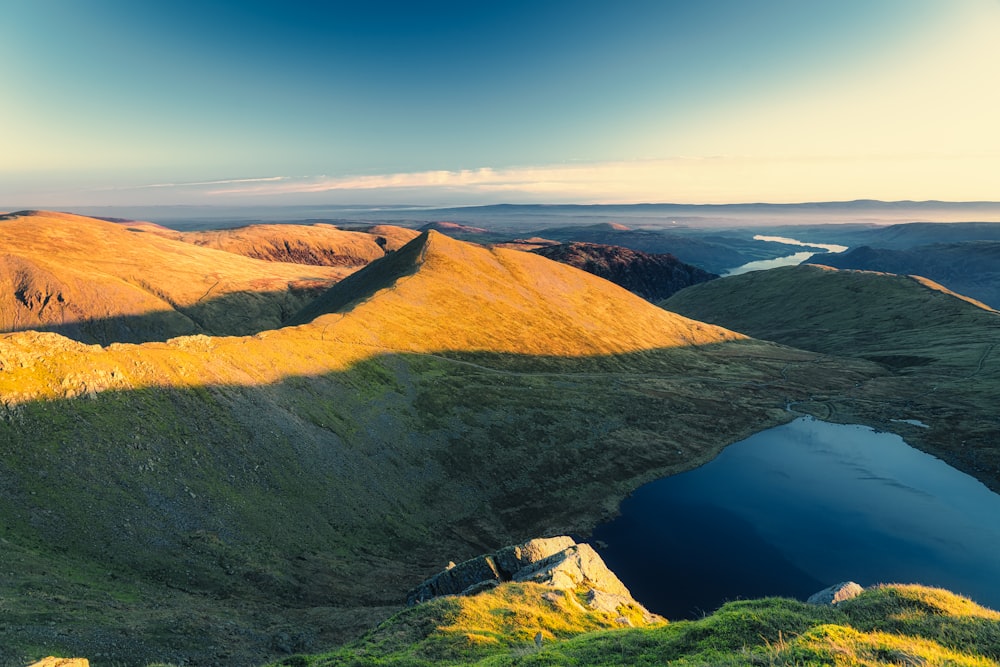 brown and green mountain beside blue lake under blue sky during daytime