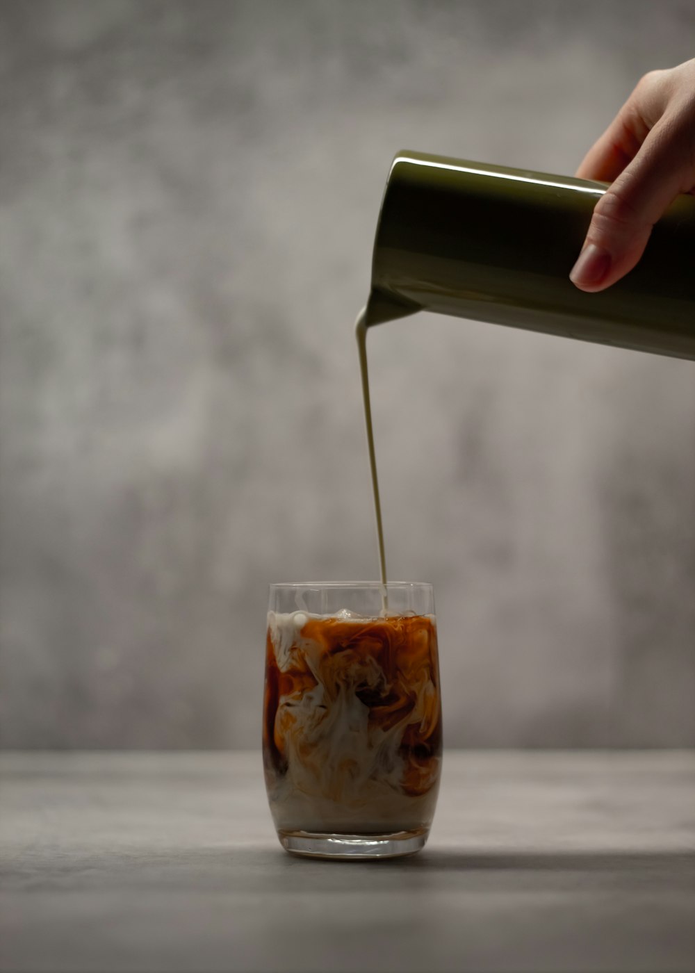 person pouring brown liquid on clear drinking glass