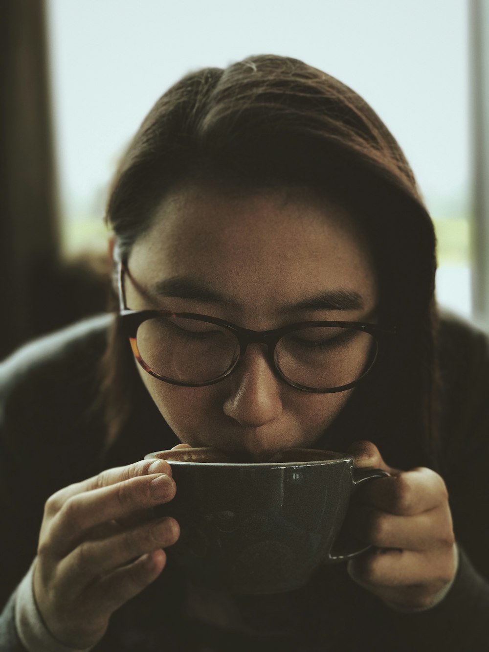 Femme en lunettes à monture noire tenant une tasse en verre transparent