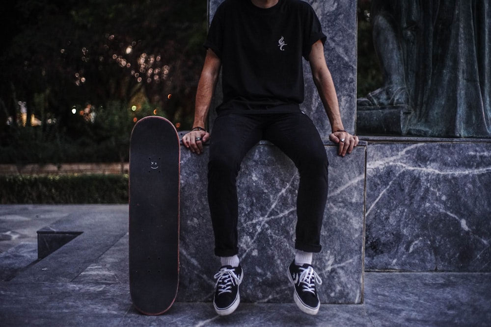 uomo in t-shirt girocollo nera e jeans in denim nero seduto sullo skateboard nero durante