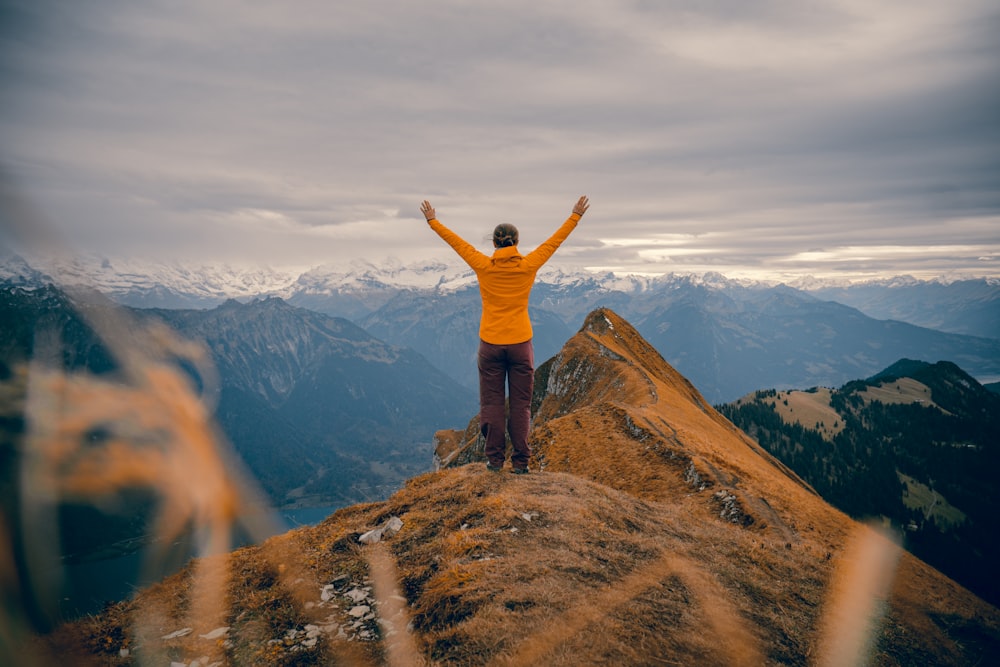 man in orange jacket standing on brown rock formation during daytime