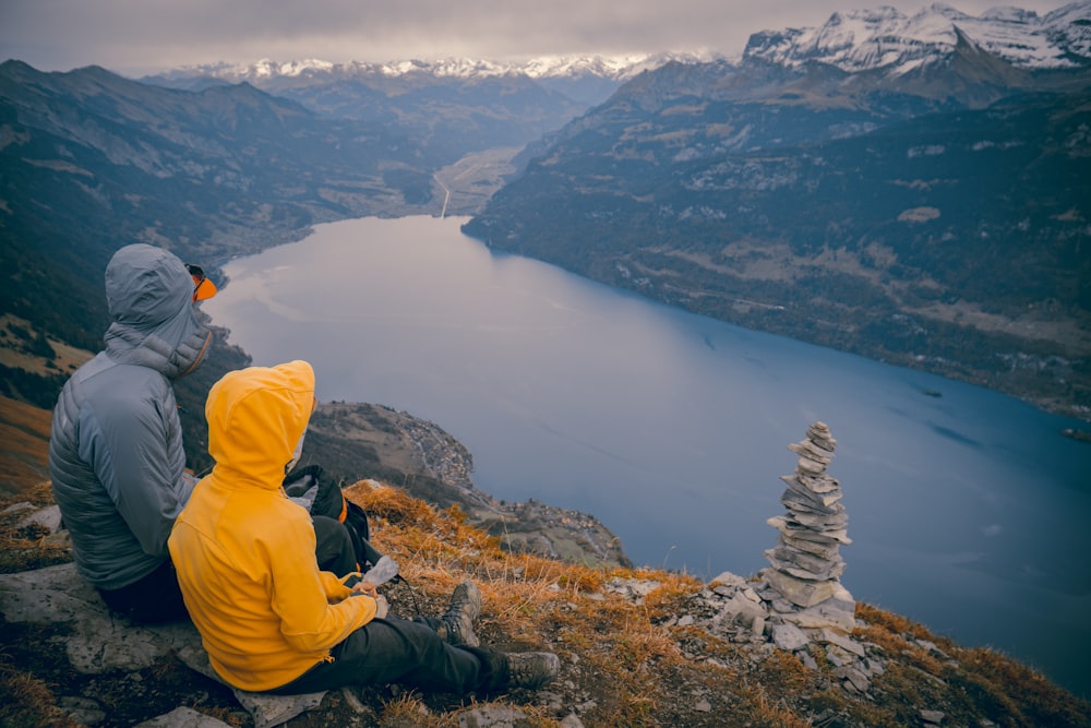 person in yellow hoodie sitting on rock formation looking at lake during daytime