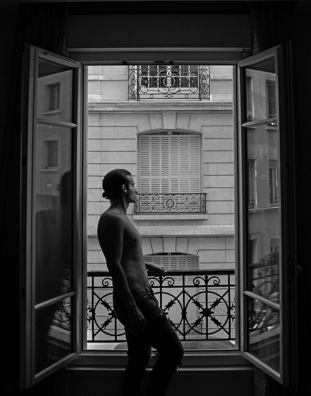 topless man in black pants and black shoes sitting on chair in front of window
