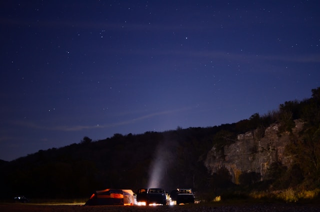 A group of off-road vehicles parked beside a campfire under a starry night sky, surrounded by dense forest.