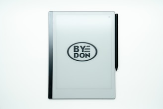 A digital tablet with an e-ink screen displays the phrase 'BYE DON' inside an oval, suggesting it might be a play on words or statement. A stylus is attached on the right side of the device.