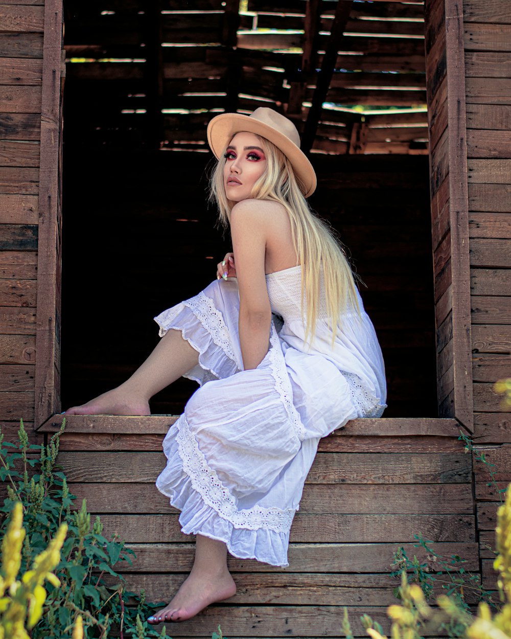 woman in white dress and brown hat sitting on brown wooden stairs