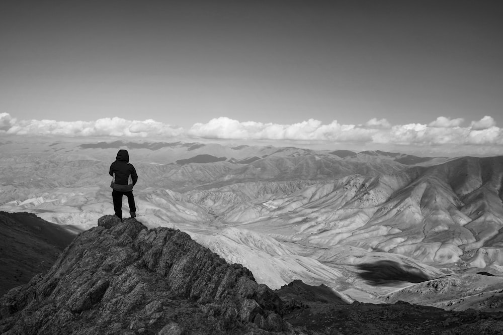 person standing on rock formation in grayscale photography
